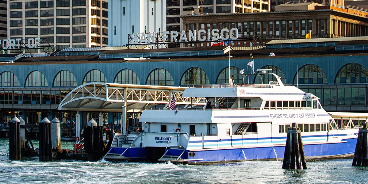 Ferry docked at the San Francisco ferry terminal. Blue and white ferry sitting at the docks with terminal in the background.